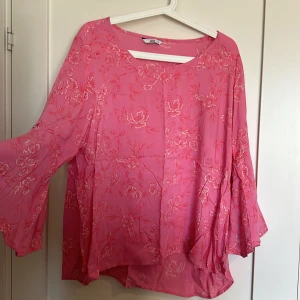 Rosa blus  - En blus i fint skick med vida armar, längre bak och kortare fram.  Djur finns i hemmet! 