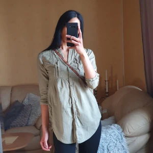 Lång skjorta  - Khaki grön skjorta med fina detaljer i bröstet, den är längre bako och går att sjystera i armarna. Har också två praktiska fickor med bra djup 👌🏽🫒 Längd fram: 78cm, Längd bak: 86cm 💯 Bomull 💯 × Jag är 173cm (xs) och alltid nytvättat innan utskick