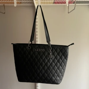 Svart guess väska - Fin väska, säljs pga att det inte är min stil längre. Litet slitage längst ned på väskan men annars i fint skick. Får plats med dator och är fortfarande väldigt rymlig! Originellt 1200, säljs för 600kr plus frakt.