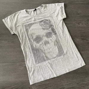 Grå tisha  - Grå T-shirt från Gina Tricot, storlek S, med ett blekt döskalletryck (det ska vara så). Använd enstaka gång. 