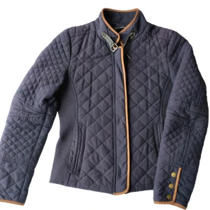 Jacka Zara Woman  -  En fin och skön quiltad, figursydd, mörkblå jacka från Zara Woman i strl medium. Med dragkedja och tryckknappar fram. Dragkedja i fickorna på sidan, resår på sidorna och mocka i ärmarna och längs med dragkedjan och kragen. I fint skick.