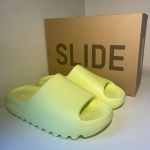 Yeezy Slide ”Glow Green” - 🚨Yeezy Slide Glow Green🚨Storlek 46, men väldigt små i storlek. Passar 43-45. Oanvända, helt nya (DS)100% Äkta, kvitto finns. Kan frakta/mötas upp. Skickar gärna fler bilder och svarar på frågor. Pris kan diskuteras! 