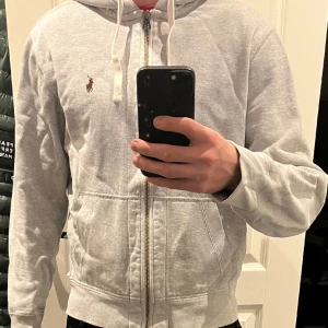Ralph Lauren zip hoddie - Säljer min ralph lauren zip hoodie i en ljusgrå färg som är i ett väldigt bra skick, inga defekter och färgen är precis som när jag köpte den. Sjukt snygg hoodie i storlek M som passar till allt!
