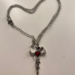 Halsband - Jättefint halsband med ett svärd, vingar och ett rött hjärta ❤️🗡️🪽köptes för ca 100kr+ men säljer ganska billigt. Köpte på en marknad, därför vet jag inget märke 