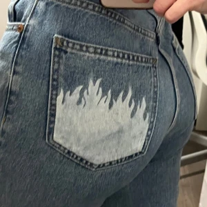 Mom jeans med flammor - Mom jeans köpta från pull & bear med vita flammor på ena bakfickan. Endast använda ca 3 gånger men de matchar inte min längd men de ser jätte bra ut när de sitter rätt. Orginalpris 299kr