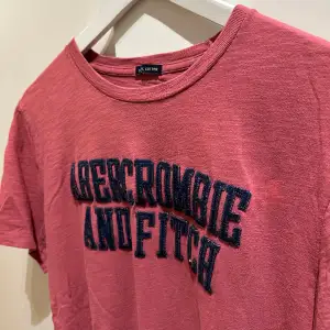 Här presenteras en ljusröd T-shirt från Abercrombie & Fitch. Tillverkad av 100% bomull med en baggy passform. Väldigt bra skick pga dess oanvändning.