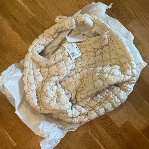 Cos quilted bag stone colour  - The quilted bag is a cornerstone of the COS collection. Designed to be slung across the body or worn on your shoulder, this oversized version has enough room for everything you need for an overnight stay, and then some. It's crafted from 100% recycle