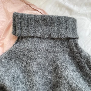 Stickad polotröja  - Mörkgrå stickad polotröja med hög krage. 5% alpacka.