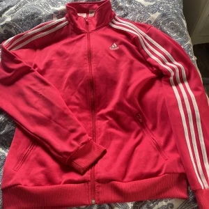Rosa adidas kofta  - Har några fläckar på sig vilket som man ser på bild 2,3 och något litet knappast ett hål men lite slit märke bedvid de vita linjerna. Annars är den bra! 