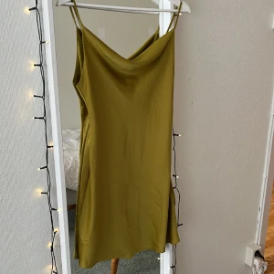 Urban Outfitters klänning - Superfin satinklänning från Urban i olivgrön färg. Använd typ 2 gånger! Passar perfekt med en tröja över så kan det se  ut som en kjol också:)