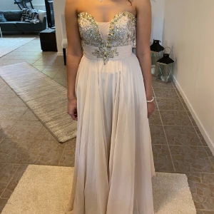 Beige balklänning med stenar - Säljer denna klänning från Shail K, endast använd en gång. Släpar lite på marken och jag är 172 cm. Finns en storleksguide från deras hemsida, skriv privat så skickar jag . Pris kan diskuteras 