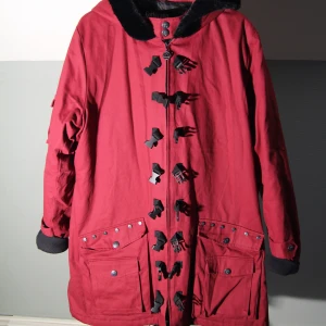 Mörkröd mellansäsongs kappa från EMP - Mörkröd mellansäsong kappa med luva  Från Gothicana by EMP  Stl. 3XL Mått enligt hemsida: Längd (baksida): 91,5cm Bredd över bröst: 66.5cm Armlängd: 68.5cm  Som ny, endast använd enstaka gånger