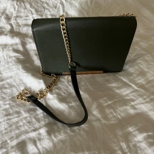 Grön väska  - Snygg axelremsväska med guldkedja!! Har tre innerfack 👛 köpt secondhand så vet ej märke  Bredd: 23,5 cm Höjd: 16 cm Djup: 7,5 cm