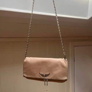 Zadig & voltaire väska  - Ljus rosa Zadig & voltaire väska med silver logga.  Dåligt skick(smuts går ej bort) (3:de bilden) och därför säljer jag den billigt. Köptes begagnat länge sen. En zandig&voltaire påse medkommer. Bara långa kedjan kvar. Org pris: 3 595 kr 