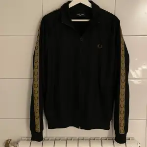 Svart och guldig Fred Perry Zip tröja i jätte fint skick, bara använd ett fåtal gånger.  Storlek: L Nypris: 1500kr Mitt pris: 699kr