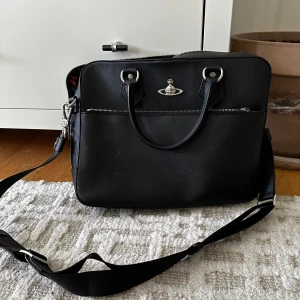 Vivienne Westwood Leather bag - En unik vivienne Westwood datorväska, svart syntetiskt läder med silver detaljer. Endast använd fåtal gånger. Älskar den mer än livet själv, men pga personliga anledningar måste den säljas. Den är rymlig och har en massa olika fack i. 