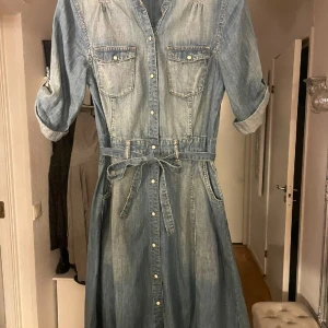 Lindex jeans klänning  - Snygg modern jeans klänning med fickor knytband och knappar i armen.. hela vägen är knappar ..snygg  blå färg med skiftningar  storlek 36 Inte använt 