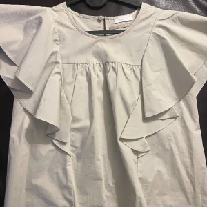 Blus  - En super fin tunn blus som är perfekt för sommar och till lite finare tillfällen. Blusen har även fina volang.  ärmar. En knapp högt upp på ryggen vid nacken. 