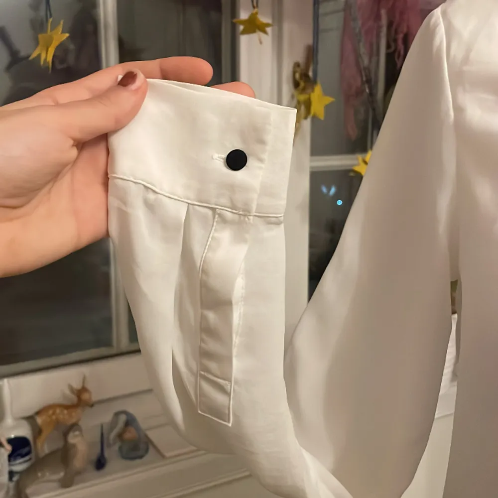 Säljer denna vita veckade skjortan med svarta knappe vid ärmarna. Den har en liten fläck vid armhålan (sista bilden) men annars är den i bra skick!. Skjortor.