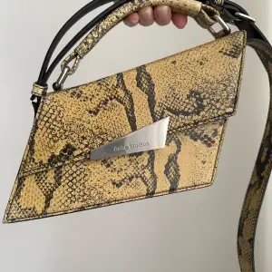 Acne Studios yellow distortion mini bag is made of python print 100% leather with a crossbody shoulder strap. It can also be carried as a handbag.   Slightly broken on left side, see images.  Width: 20 cm Height: 14 cm (with handle)  Depth: 9cm