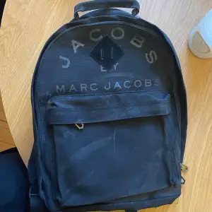 Svart ryggsäck från Marc by Marc Jacobs i tyg med mockadetaljer. Har aldrig använt denna, så i nyskick. Rycksäcken har legat nedpackad, därav lite dammig.