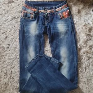 Snyggaste jeansen!! - Jeans som är ovanliga  med massa detaljer..massa paljetter både fram och bak snygga knappar låg midjande ..fickor fram bak snygga slitningar storlek 26 passar xs s väldigt fint skick!