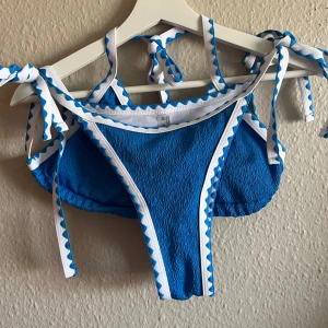 Blå bikini med vita detaljer - Säljer en superfin blå bikini med vita detaljer. Överdelen har en triangelmodell med knytband runt nacken och ryggen. Underdelen är en klassisk trosa med knytband på sidorna. Båda delarna har en ribbad textur och är superbekväma. Perfekt för sommarens alla badäventyr! 💙aldrig använd 