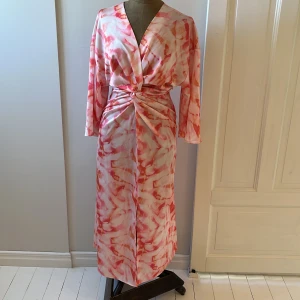 Färgglad klänning med slits - Säljer en superfin klänning från Kappahl i storlek M. Klänningen har ett mönster i rosa toner, perfekt för sensommarens mingel och fester! Den har vida trekvartsärmar och en snygg drapering i midjan, dragkedja i sidan. Aldrig använd. Nypris 800 kr.