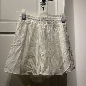 Vit kjol från BikBok - En vit kortkjol från BikBok med elastisk midja. Kjolen är tillverkad i ett lätt och luftigt material, vilket gör den perfekt för varmare väder.