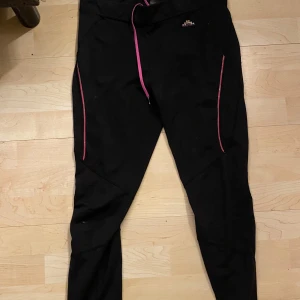 Svarta träningsbyxor med rosa detaljer - Säljer ett par svarta träningsbyxor med rosa detaljer. Byxorna har en snörning i midjan och dragkedjor vid fickorna. Perfekta för träning eller en aktiv vardag. De är i bra skick och väldigt bekväma.