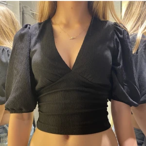 Svart croppad topp med puffärmar - Säljer en snygg svart croppad topp med puffärmar. Toppen har en v-ringad hals och är tillverkad i ett ribbat material som ger en skön passform. Perfekt för fest eller en utekväll! 🖤Köpt på gina tricot ❣️