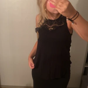 Svart ärmlös topp med spetsdetaljer - Säljer en snygg svart ärmlös topp i storlek S. Toppen har fina spetsdetaljer vid halsen och är perfekt för både vardag och fest. Den är tillverkad i ett mjukt och bekvämt material som känns skönt mot huden. Passar bra till både jeans och kjol!