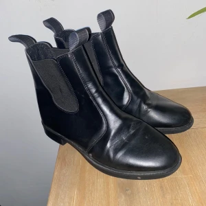 Svarta Chelsea boots i skinn - Säljer ett par svarta Chelsea boots i skinn. De är i bra skick och har en klassisk design med elastiska paneler på sidorna för enkel på- och avtagning. Perfekta för höst och vinter!