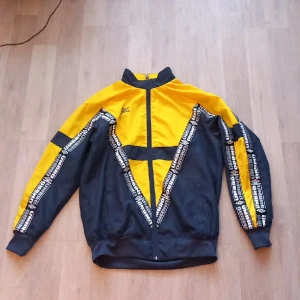 Gul och Mörkblå Umbro jacka - En snyggjacka som passar till streetwear och hade passat perfekt till ett par mörkblåa jeans. Det är en tunn vindjacka och har storleken Medium. Pris kan diskuteras.