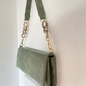 En grön väska från Åhléns. Man kan ha väskan över axeln som en pochette väska, men man kan även ta av bandet och ha väskan som en kuvertcäska. Köparen Står för frakten, inga returer 🥰