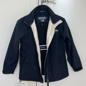 Sebago vårjacka barn - Marinblå jacka från Sebago, lätt fodrad vindtät. Storlek 134/140. Fint skick. (Märkeslappen på insidan är sliten men syns inte när jackan är på.)