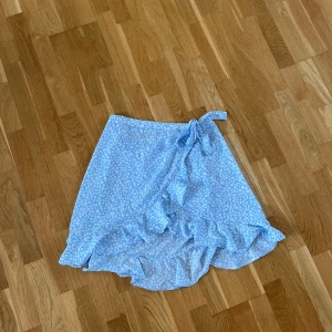 Kjol - Ljus blå kjol med vita blom och volang detlajer. Aldrig använd. Snörning som går att knyta.