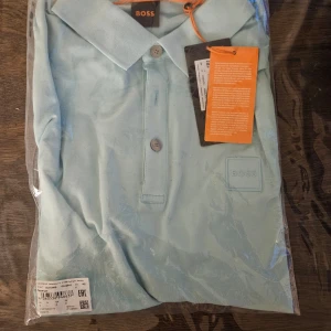 Boss kortärmad Piké - Helt ny och oöppnad Pikè från Boss i storlek L och ljusblå färg. Vid frågor är du välkommen att kontakta mig.