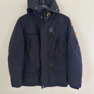  Right Hand Base Parajumper jacka junior 14 år - Marin blå höst/vinter junior jacka med huvan i storlek M (14 år) Den är lätt vaddering med dun, ärmarna med snölås och massor av stora och små fickor och mycket bra skick. Modell: Right hand base 