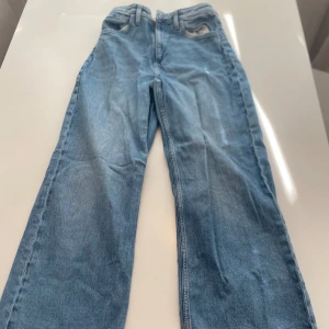 Blå jeansbyxor - Ett par blå jeansbyxor i klassisk stil. Byxorna har en rak passform och är tillverkade i denim. De har fickor både fram och bak samt en knapp- och dragkedjestängning.