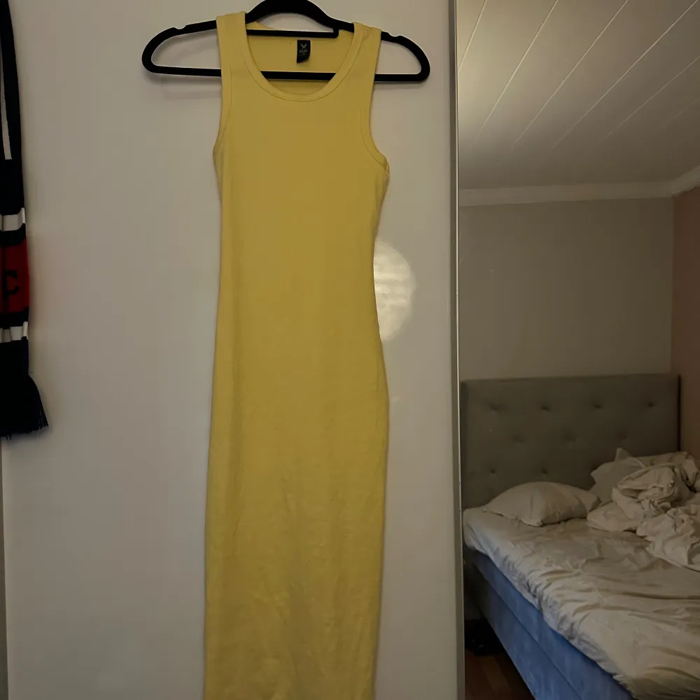 En gul ärmlös klänning med rund halsringning. Lite ljusare gul i verkligheten inte så skrikig som på bilden skulle jag säga . Mekot.