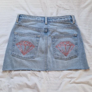 Kjol med rhinestones på bakfickorna  - Jätte fin jeanskjol med ljusrosa rhinestones på bakfickorna. Jag själv har satt dit dem med ordentligt lim. Midjemått tvärs över: 34,5cm Längd: 31cm. En jeanskjol från HM i storlek 34 som jag gjort om. Skriv till mig först om du är intresserad🫶🏻💕