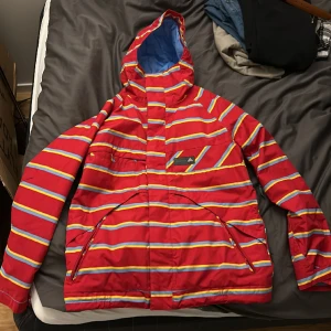 Snowboard/skidjacka Burton - Burton Snowboard Jacket Poacher (Red,Yellow,Blue).  Skid/snowboard-jacka med snöskydd från Burton. Storlek: M (fits true to oversized size) Skick: 9/10 (använd fåtal gånger, nyskick) Inköpspris: 1099:-