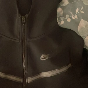 Svart Nike tech - säljer pågrund av att det itnr är min stil, okej skick men de små banden vid dragskedjan har gått av och även lappen inuti har försvunnit pga tvättning. men utseendemässigt bra skick, skriv för fler frågor 💕