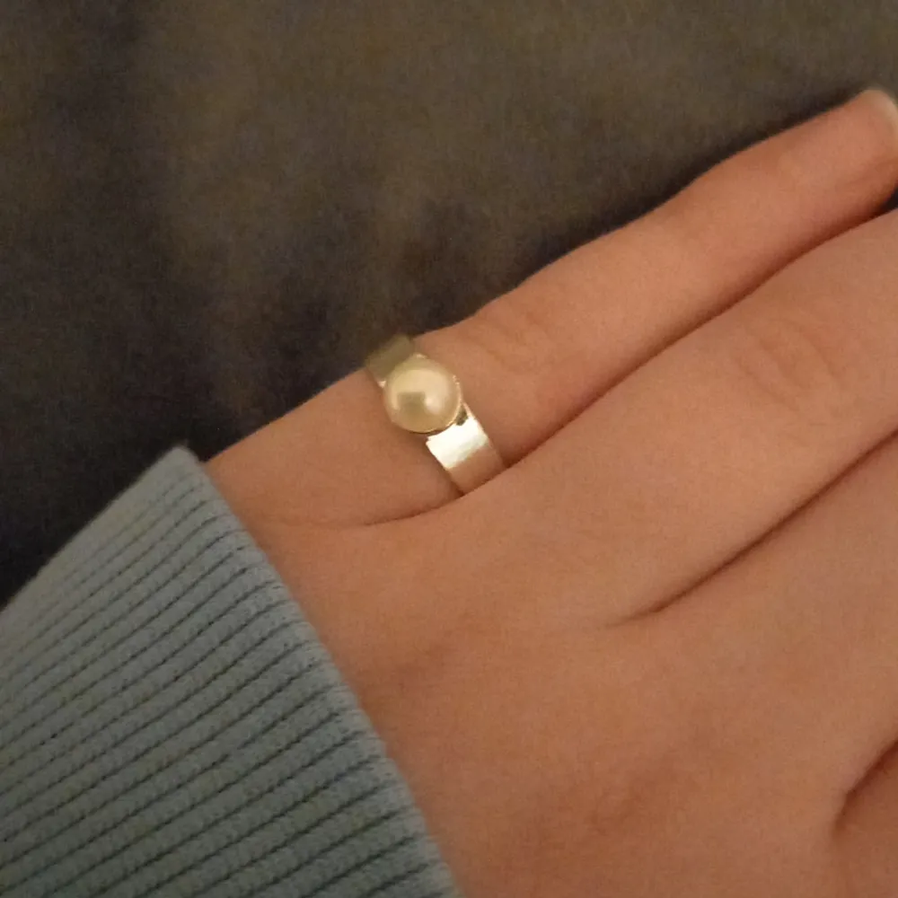 En silverring med en pärla på sig. Den är 1,7 cm bred runt hela ringen.. Asusteet.