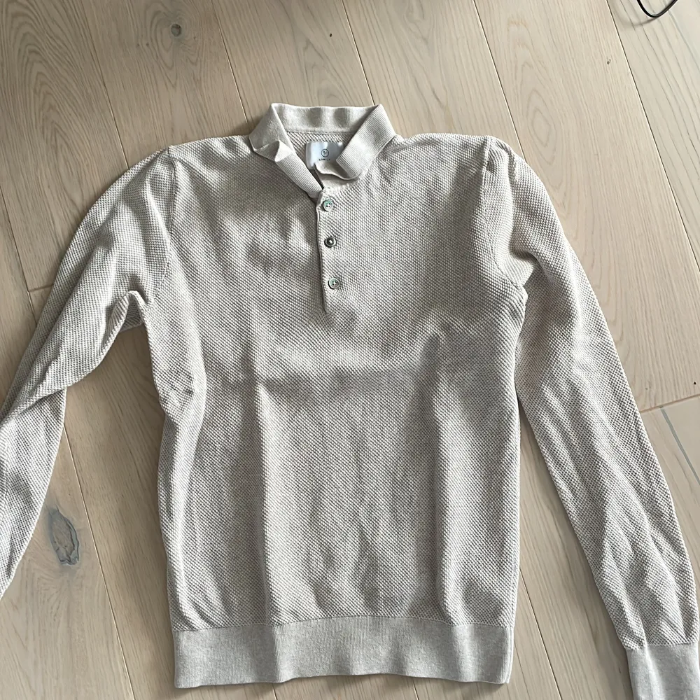 Säljer en stilren beige pikétröja från Bläck i mycket bra skick. Tröjan har långa ärmar och knappar framtill, perfekt för både vardag och lite finare tillfällen. Materialet känns mjukt och bekvämt, vilket gör den idealisk för vår och höst. Passar perfekt till jeans eller chinos!. Tröjor & Koftor.