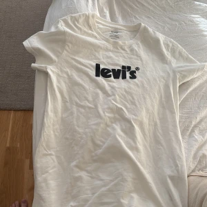 Vit t-shirt från Levi's - Säljer en klassisk vit t-shirt från Levi's i storlek XS. Den har en svart logga på bröstet och är gjord i mjuk bomull. Perfekt för en avslappnad stil eller som basplagg i garderoben. Kortärmad och i mycket bra skick!