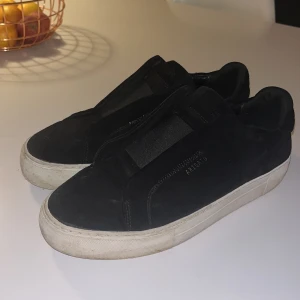 Svarta sneakers från Axel Arigato - Säljer ett par svarta sneakers från Axel Arigato i bra skick. De är gjorda av mocka och har en stilren design utan snörning. Perfekta för både vardag och fest! Sulan är vit och ger en snygg kontrast till det svarta. Lite fläckigt vid sulan men inget man tänker på. 
