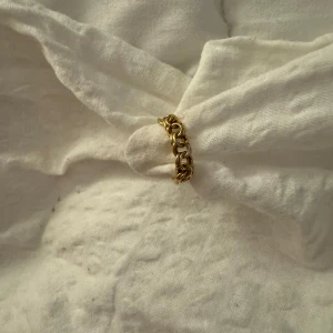 Guldfärgad ring med kedjedesign - Säljer en snygg guldfärgad ring med en unik kedjedesign. Perfekt för att ge din outfit en cool och trendig touch. Ringen är i mycket bra skick och passar till både vardag och fest. Ett måste för alla som älskar stilrena smycken!