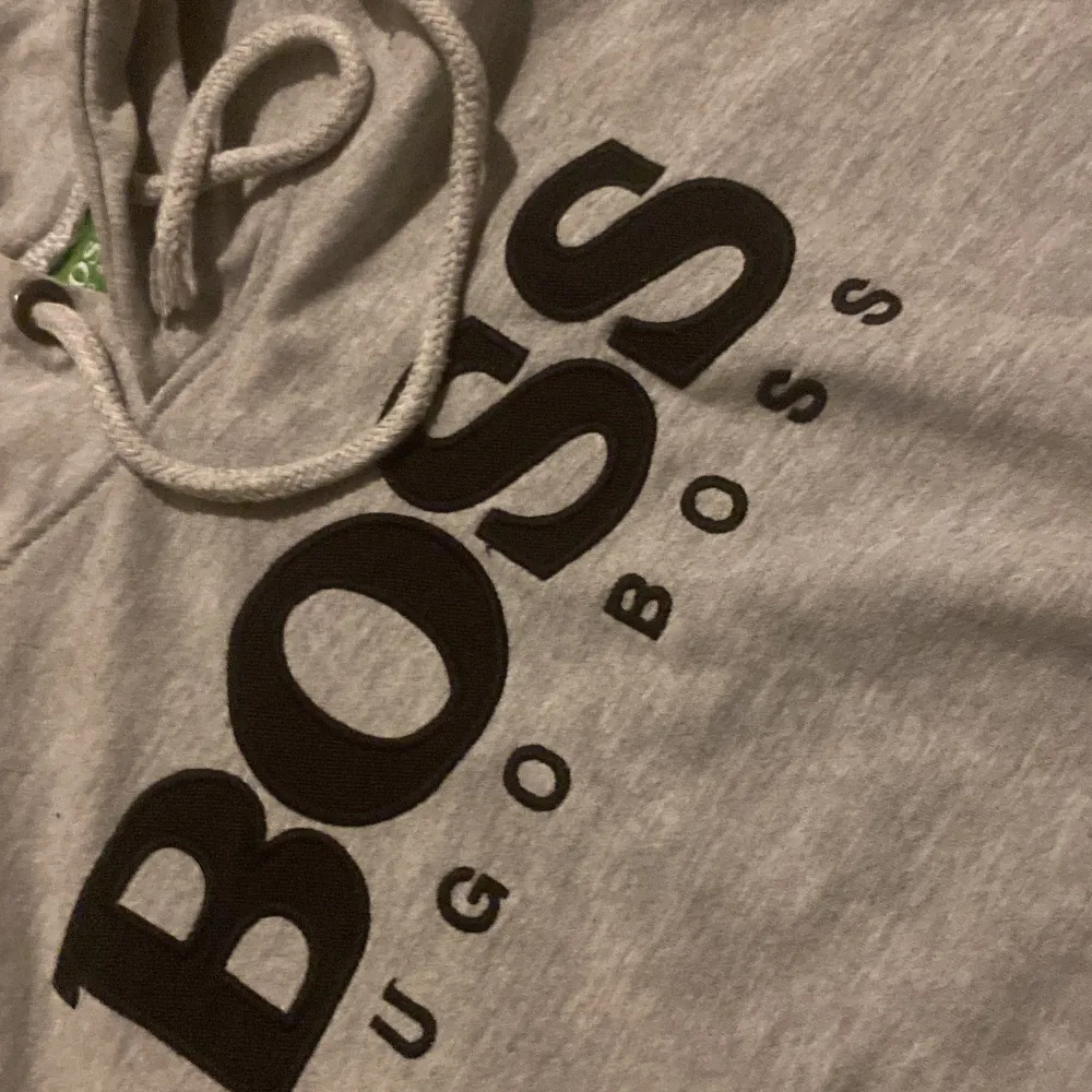 Säljer en snygg grå hoodie från Hugo Boss i mycket bra skick. Den har en stor BOSS-logga på bröstet och en praktisk magficka. Perfekt för både vardag och chill. Huvan har  passform. Passar perfekt till höst och vår!. Tröjor & Koftor.